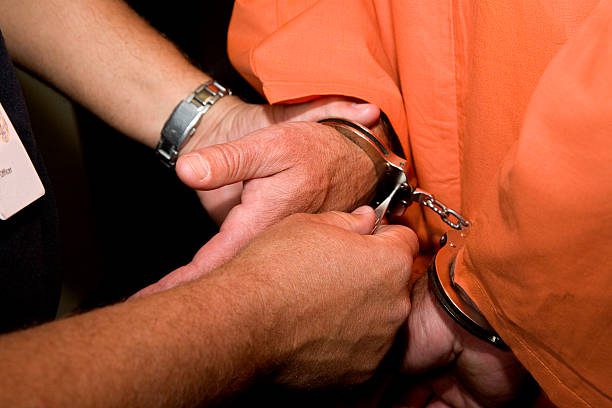 A man in an orange shirt is holding onto some handcuffs.