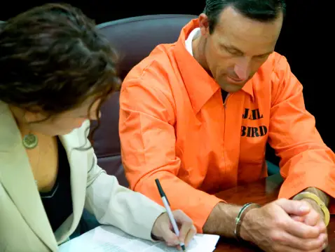 A man and woman writing on paper in an orange jail uniform.