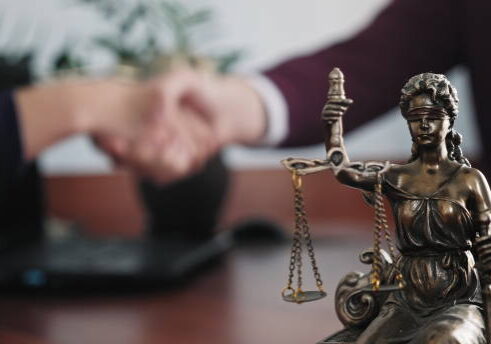 A person shaking hands over a statue of justice.