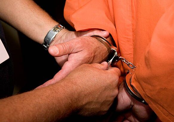 A man in an orange shirt is holding onto some handcuffs.