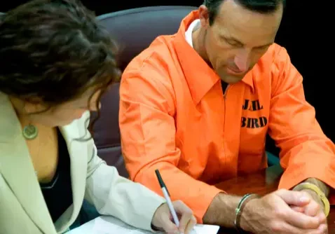 A man and woman writing on paper in an orange jail uniform.